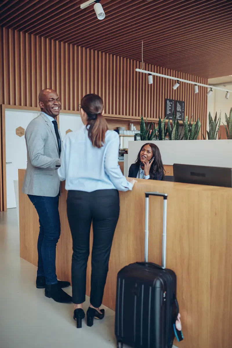 Two laughing guests checking in together at a hote muxssnk